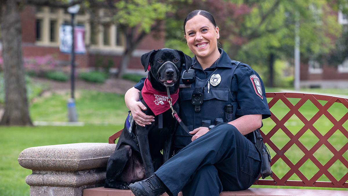 A police office and a dog, seated on a bench.