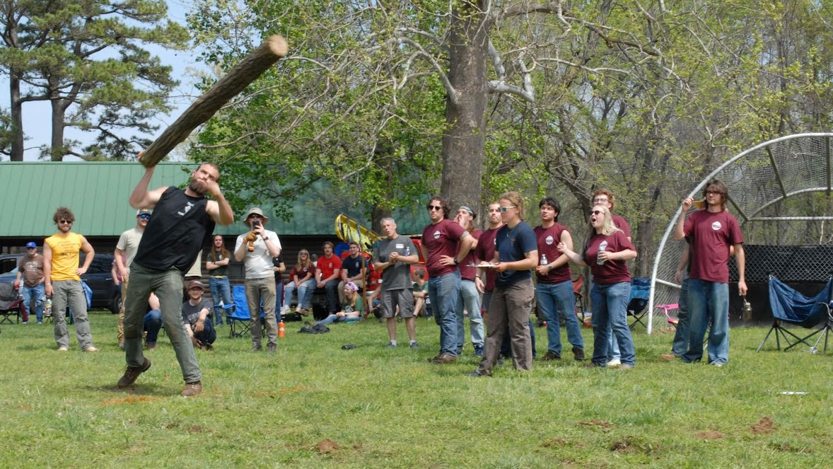 SIU Carbondale timber sports member throwing a log while other members cheer him on..