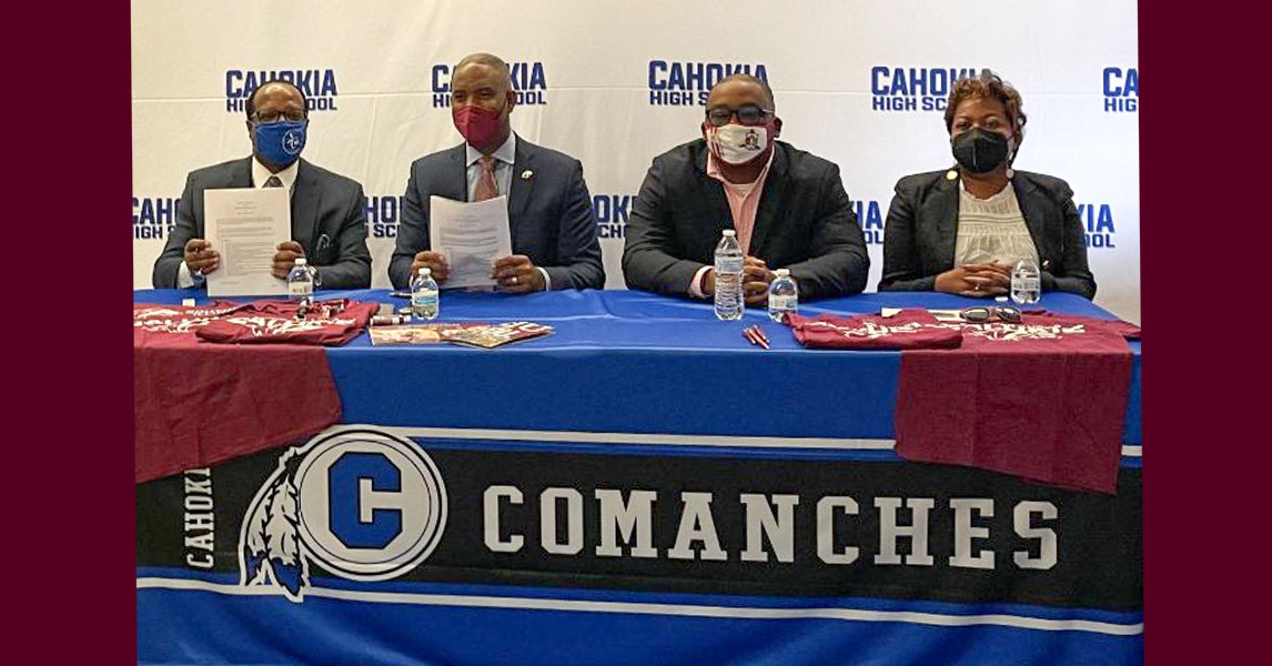 three men and one woman seated at a table wearing masks