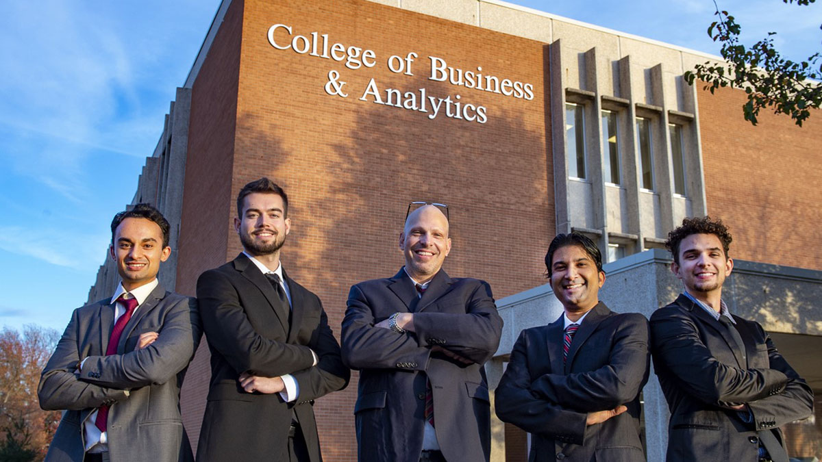 five people posing in front of a building that says College of Business and Analytics