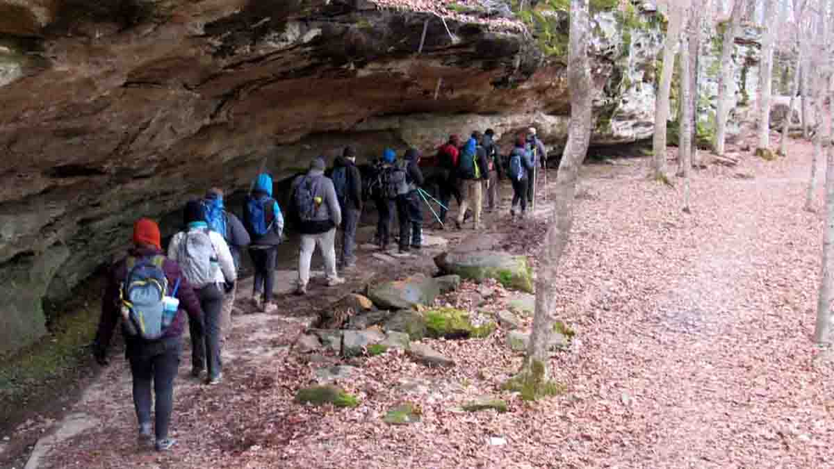 group of people walking near a rock formation, in the woods