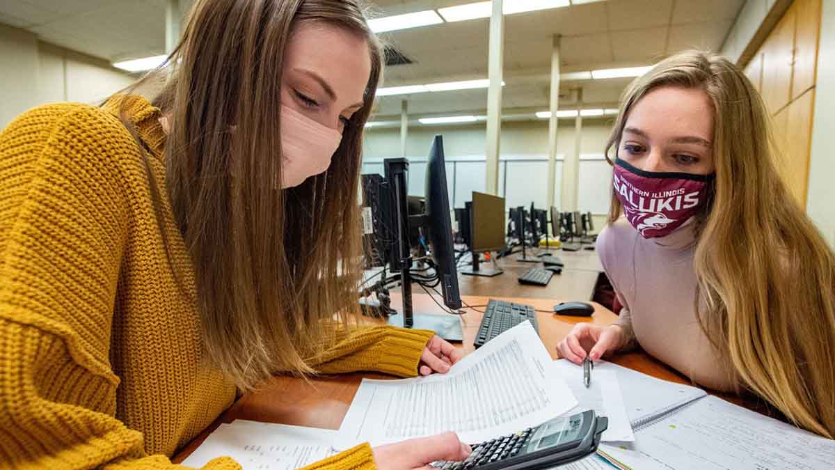 two young women wearing masks, working on taxes