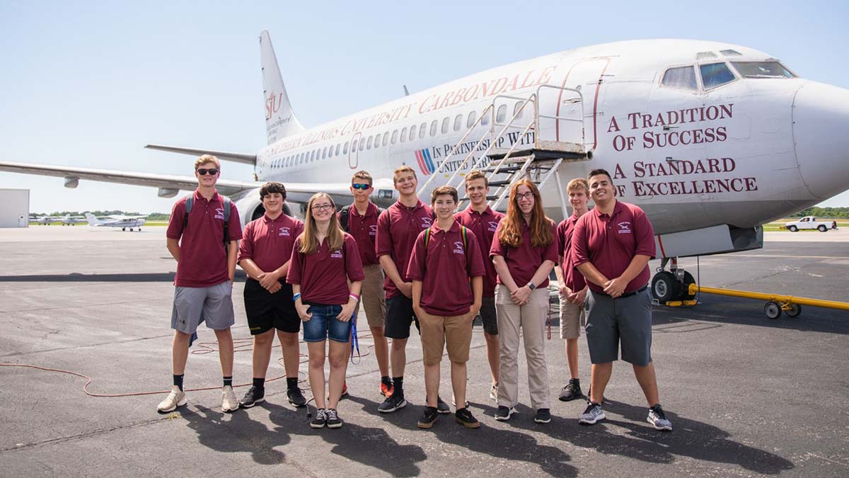 group of students standing in front of a large jet