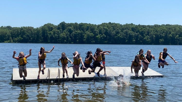 children jumping into a lake from a dock