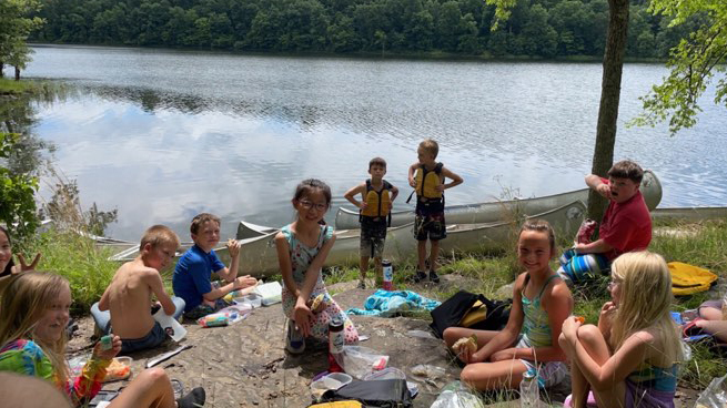 children having a picnic beside a lake with canoes in the background.