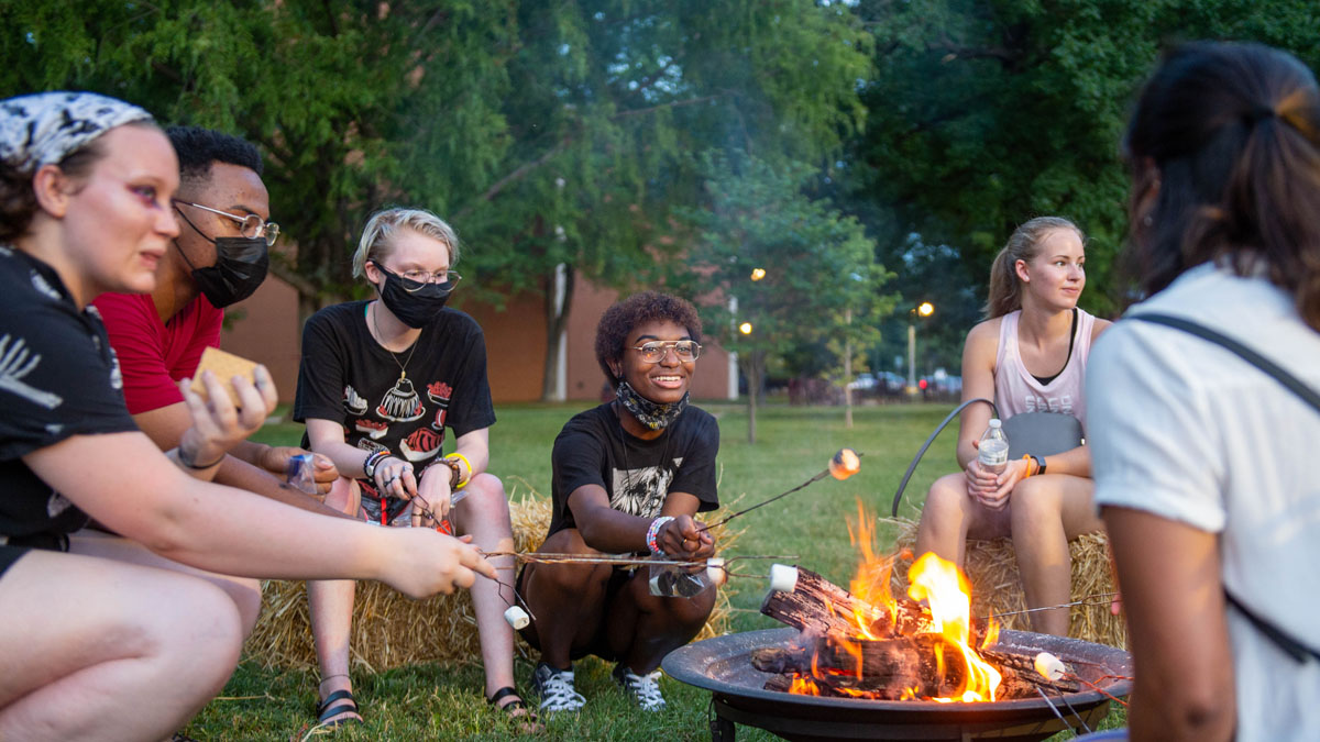 students gathered around a fire, roasting marshmallows