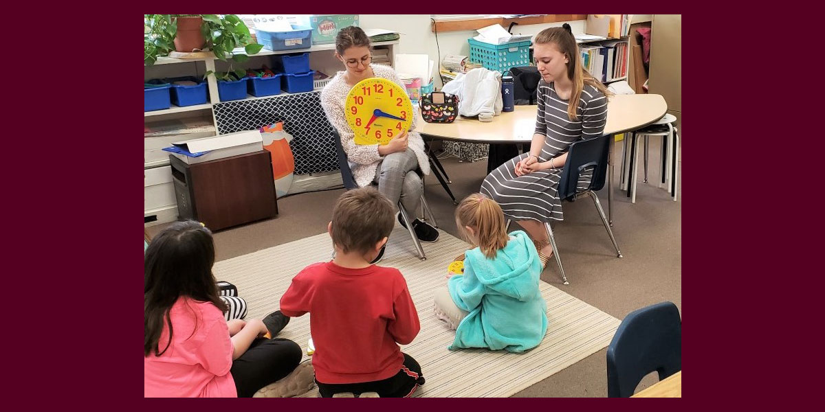 two young women are reading to a group of school children