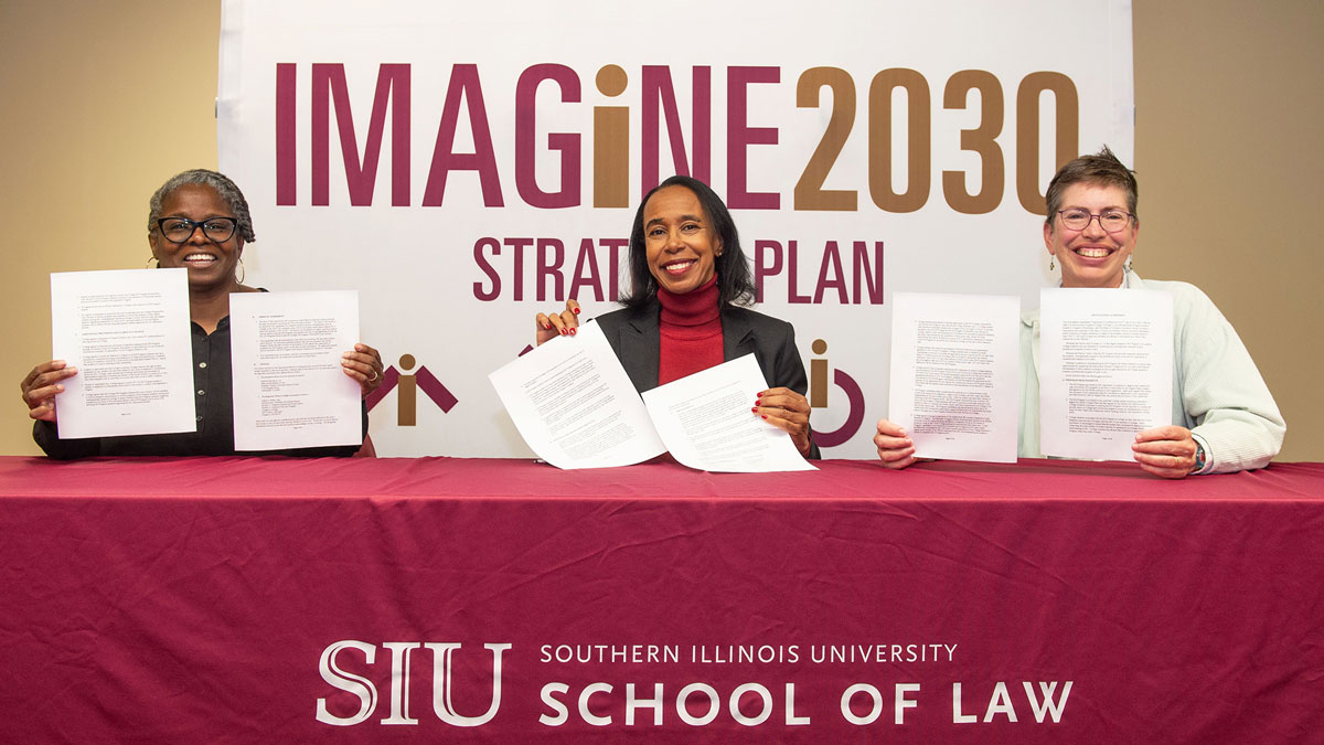 Two black women and one white woman, smiling, holding documents