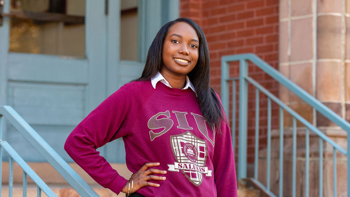 young black woman, smiling at the camera while standing on steps. She is wearing an SIU shirt.
