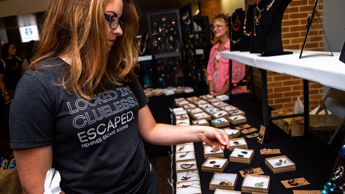 A woman is browsing a jewelry vendor at a craft sale.