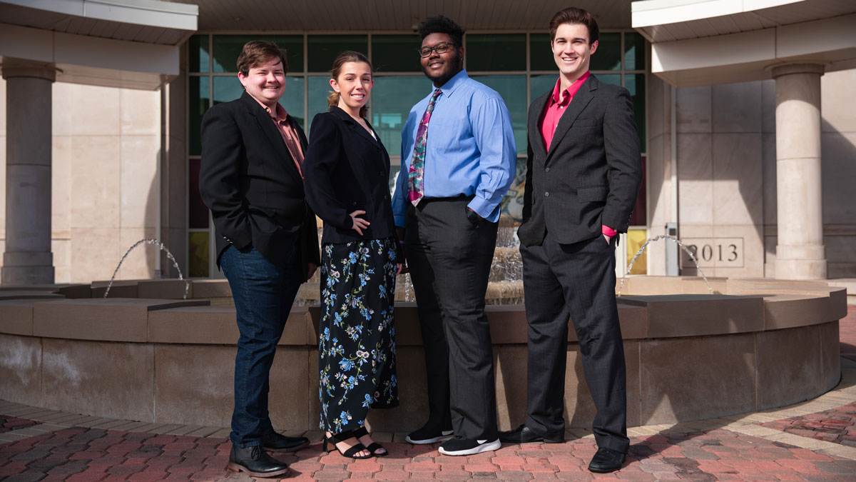 Four professionally dressed college students, posing in front of a building