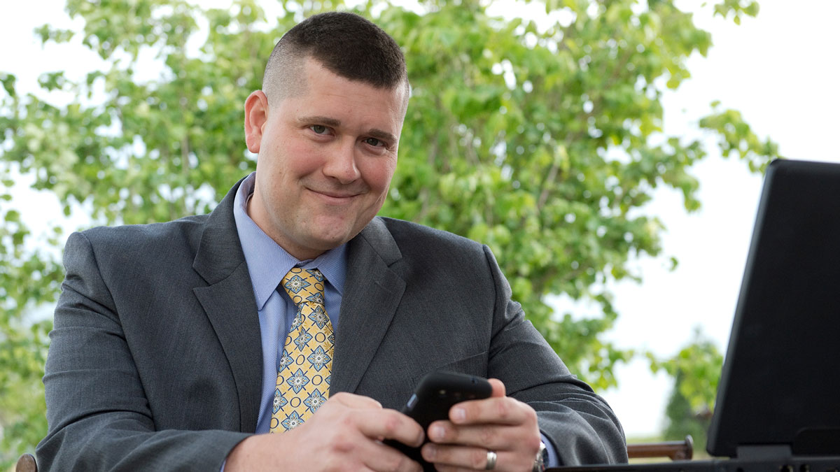  man wearing a suit and tie, a cell phone in hand, and smiling at the camera