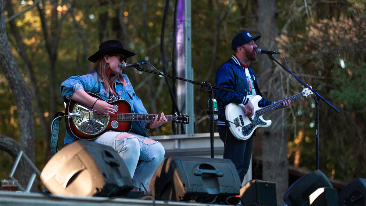 a woman and man are playing guitars and singing while standing on a stage