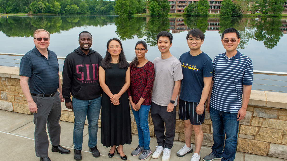 Members of an SIU research team stand in front of Campus Lake. Thompson Point is visible in the background.
