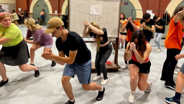 A group of men and women rehearse a dance scene.