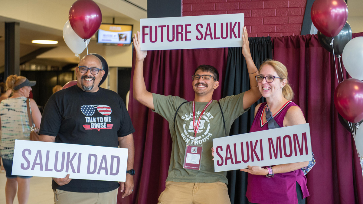  A family is smiling for pictures while holding signs that read Saluki Dad, Future Saluki and Saluki Mom