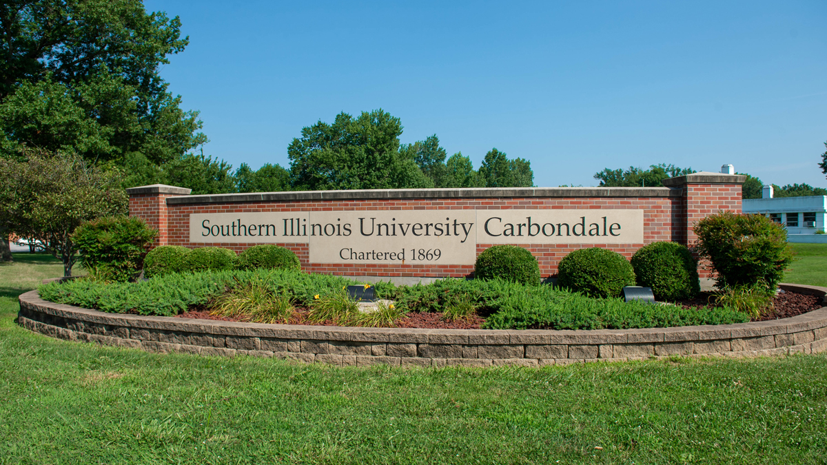 A short brick wall is in a flower bed and Southern Illinois University Carbondale, Chartered 1869, is carved into the wall.