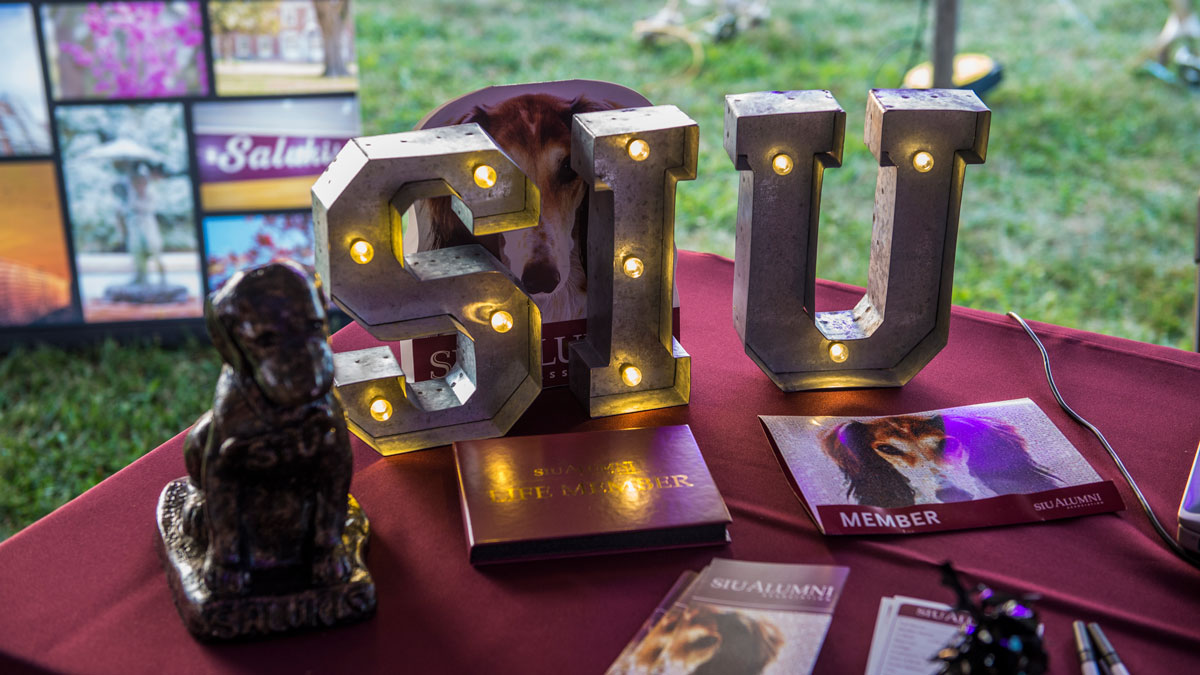 A light up sign is seen on a table with a dog statue. The sign says S-I-U.