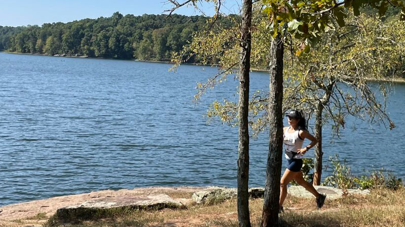A person running a race on a dirt path. A lake is visible in the background.