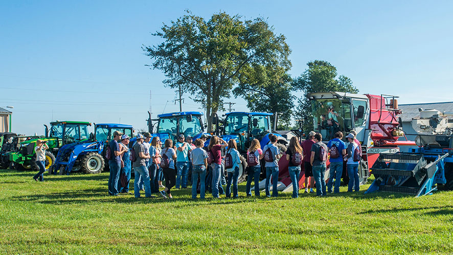 students in a field, looking at tractors