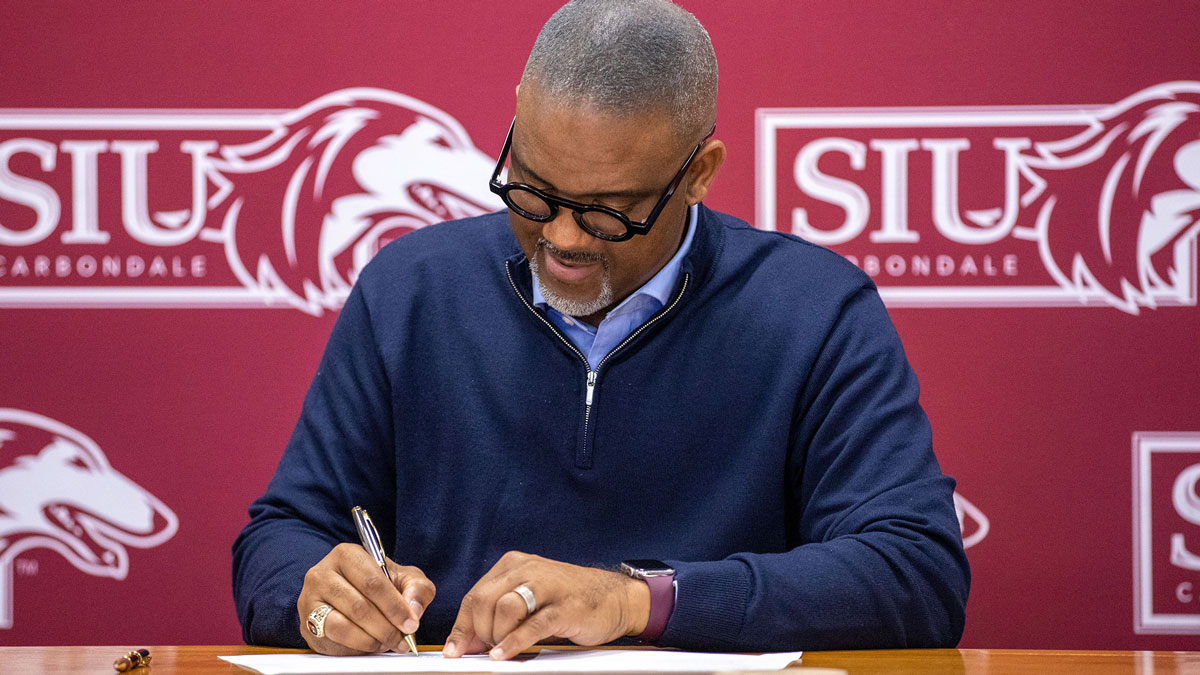 Chancellor Austin Lane is seen signing a piece of paper. His head is looking down as he signs.