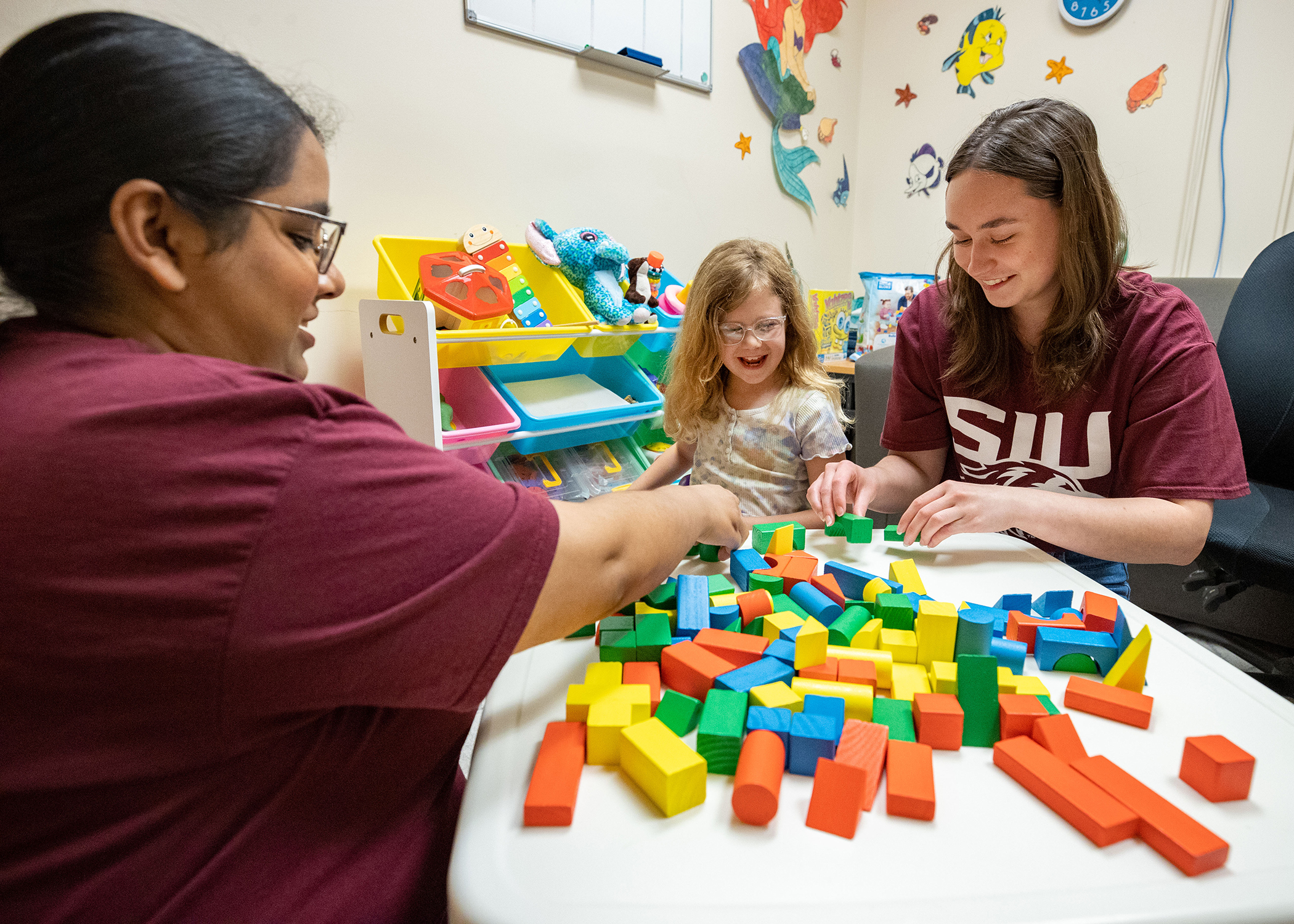 Two students are playing blocks with a client.