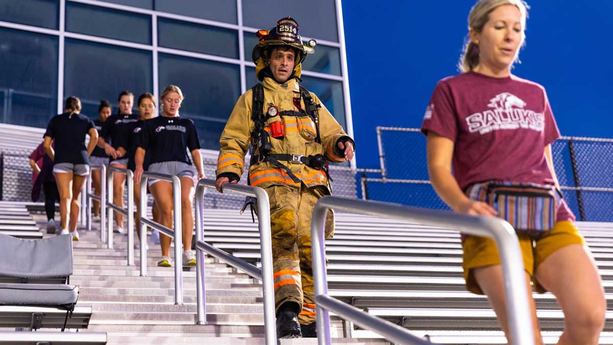 Several people and a firefighter are climbing steps at Saluki Stadium for the Saluki Stair Climb