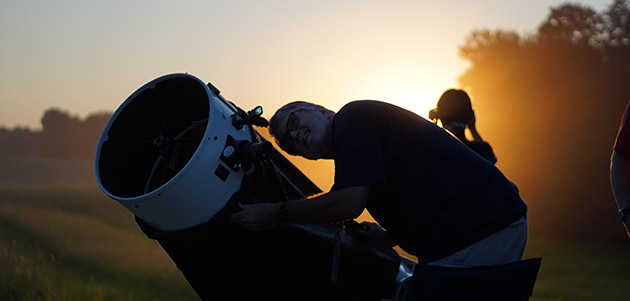 A person is seen looking through a telescope at sunset