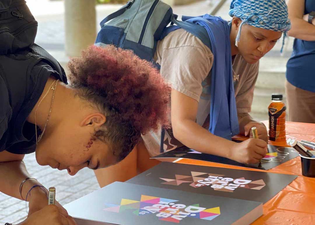 Two black women are leaning over a table while working on an art project.