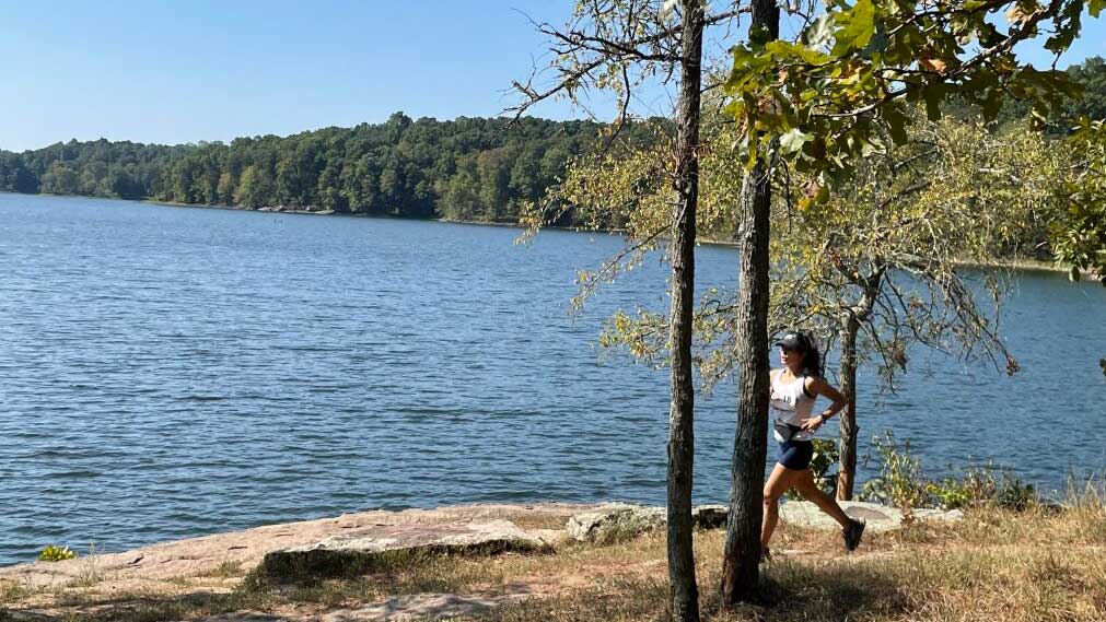 A woman is running along the banks of a lake.