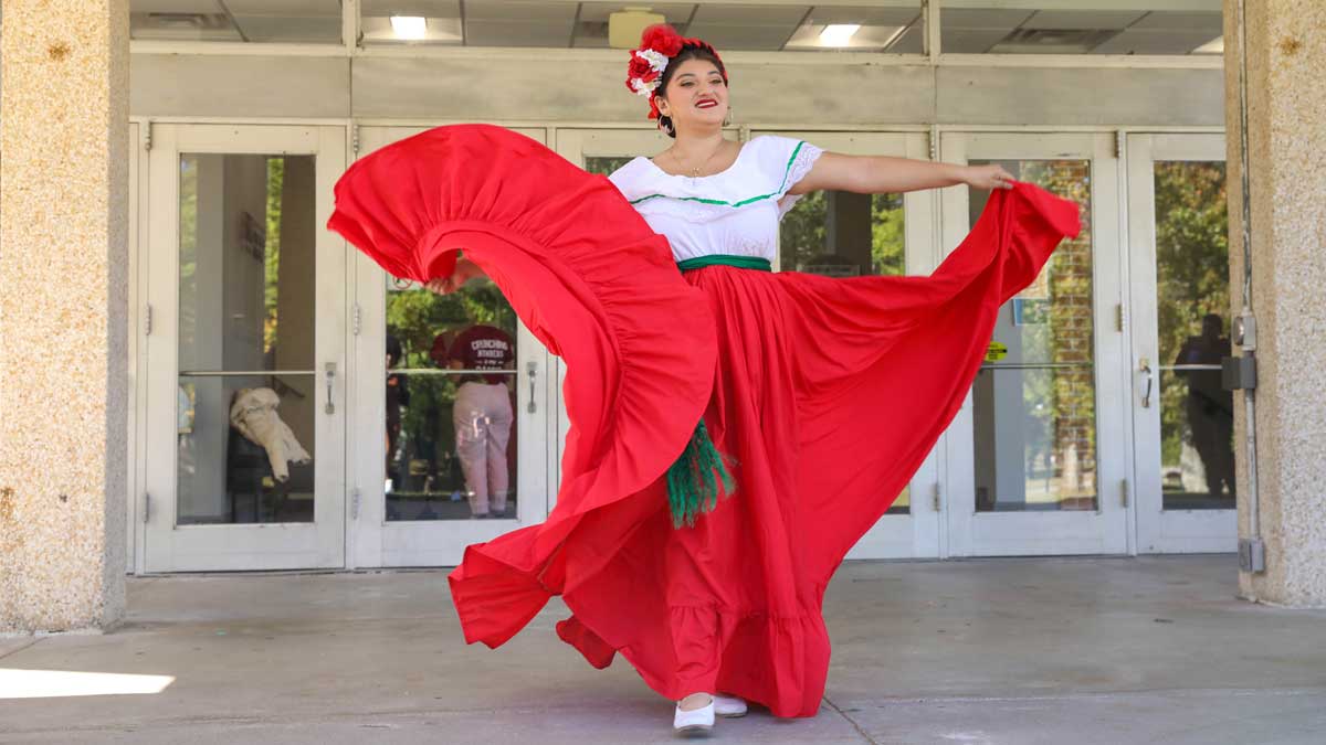  A young woman is performing a dance wearing traditional hispanic clothing, including a red skirt. 