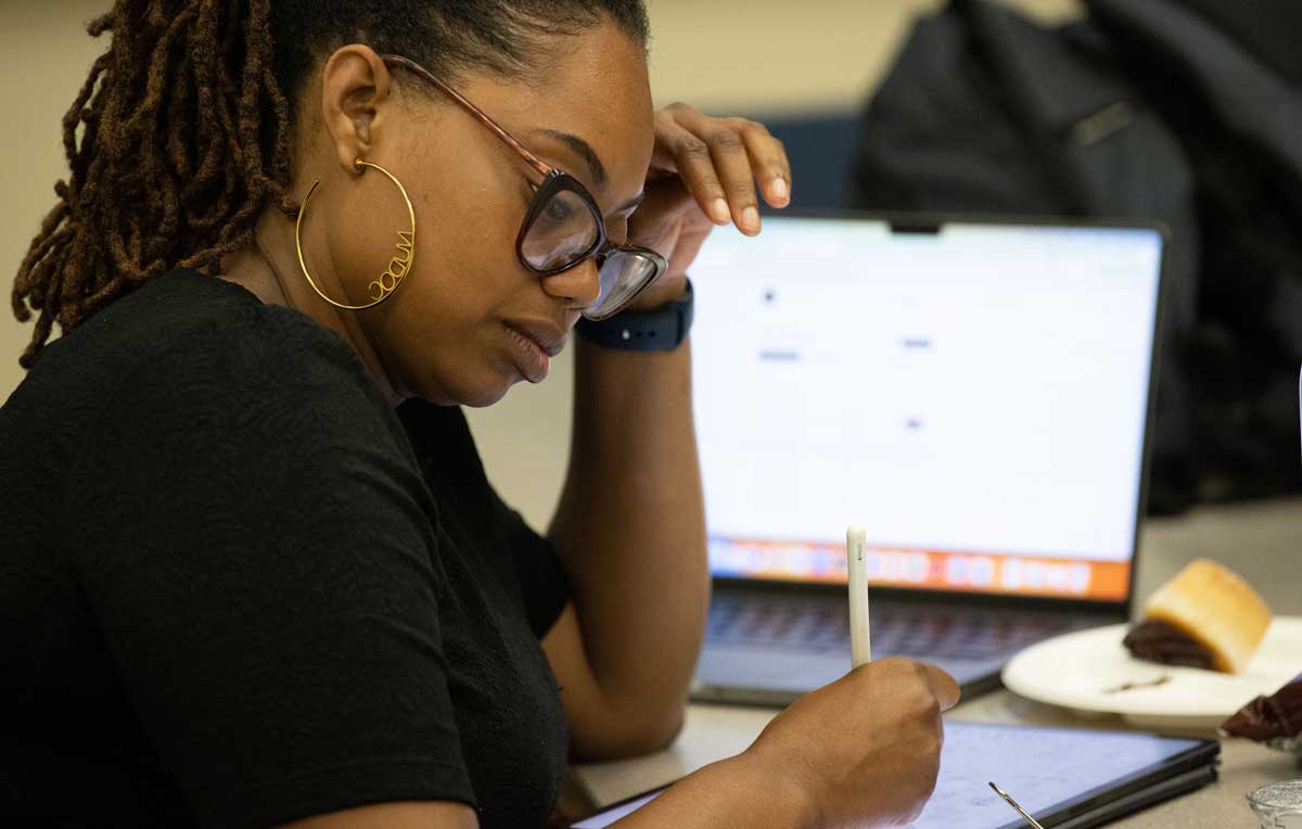 A black woman is writing with a computer visible in the background