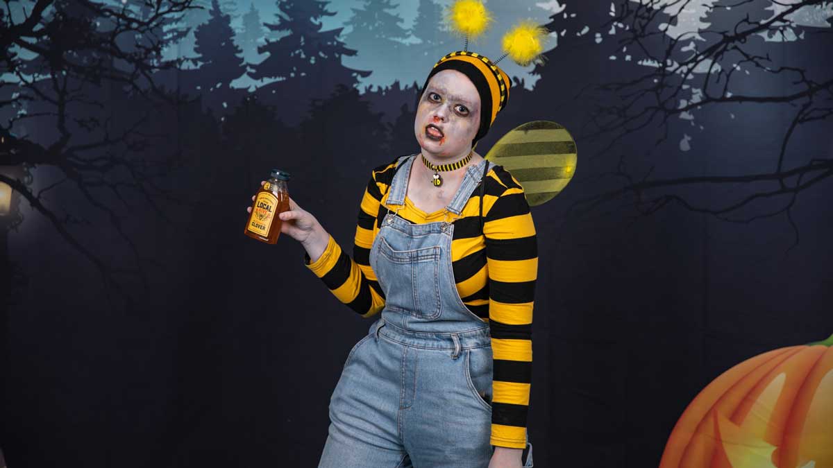 A girl dress like a zombie bumble bee, holding a jar of honey.