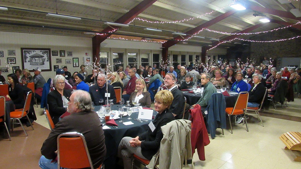 A large group of people are seated around tables in a large room.