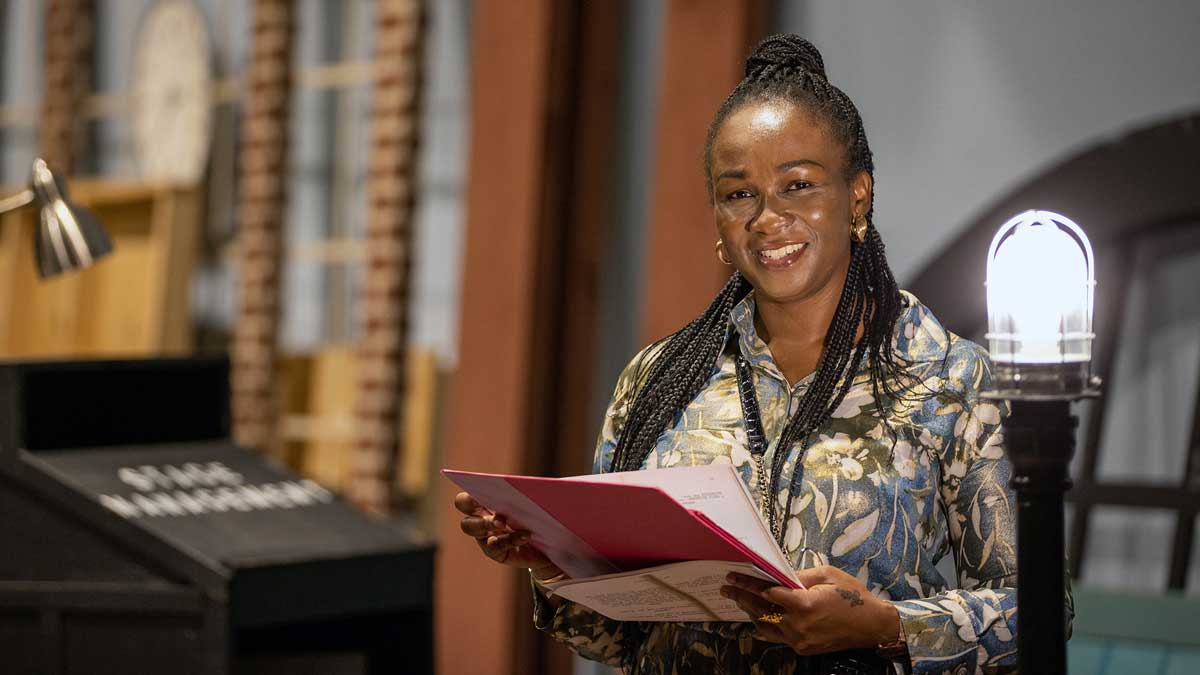 A woman stands on a stage, holding a book. 