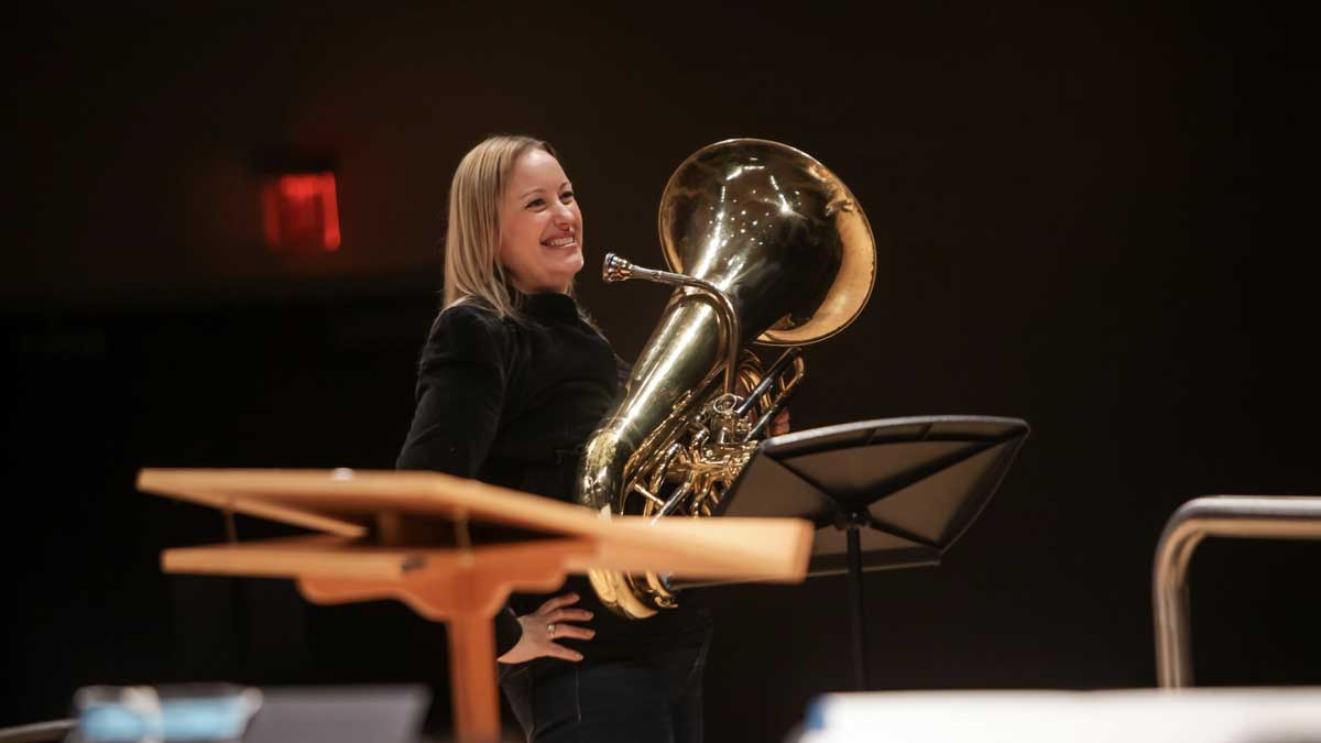 Joanna Ross Hersey is standing on a stage, holding a brass instrument.