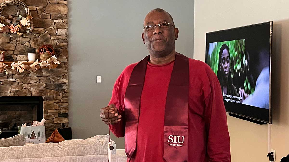 A man is trying on his graduation stole from SIU Carbondale.