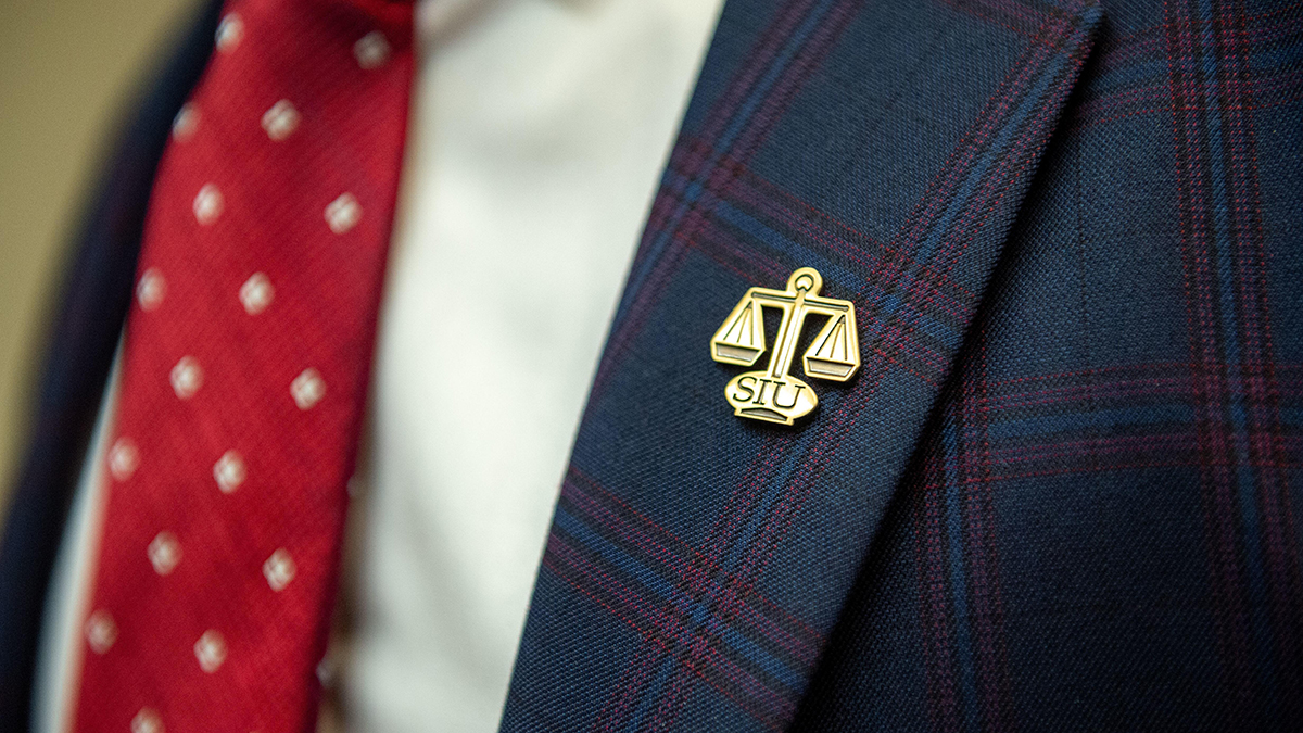 A lapel pin that is SIU with the scales of justice.