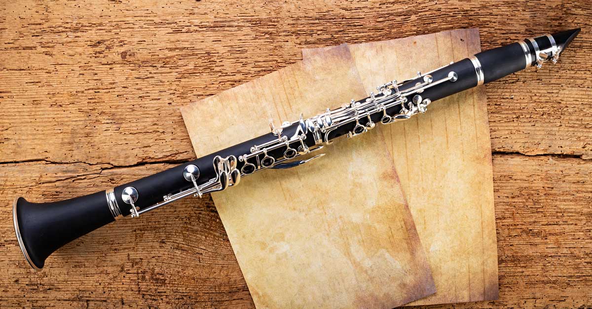 A clarinet laying on a wood surface and sheets of paper.