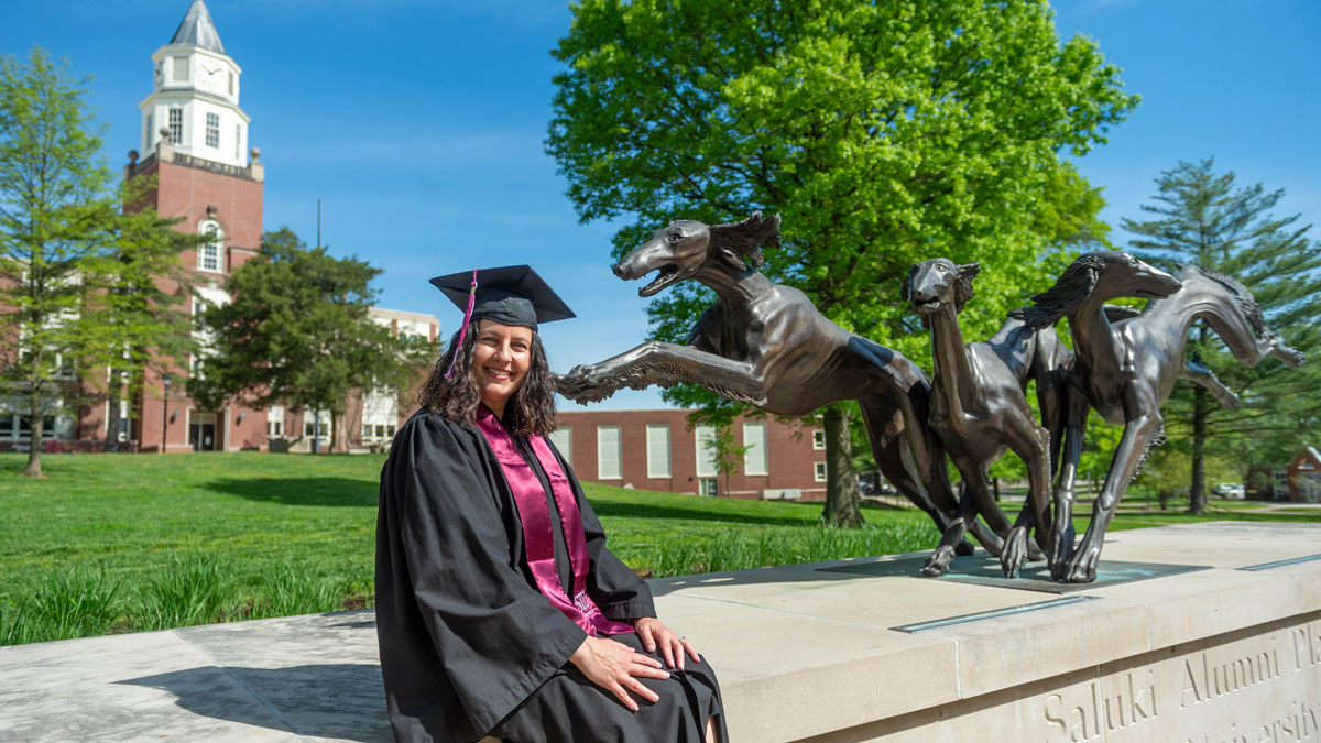 A woman seated by a saluki statue. Pulliam clocktower is visible in the background.