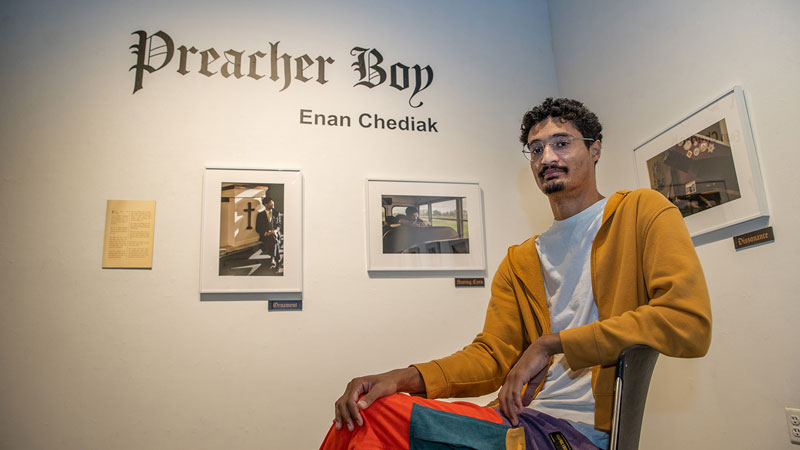 A man seated in front of his exhibit of photographs.