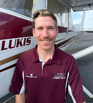A young man smiles next to an airplane.