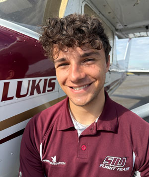 A young man smiles next to an airplane.