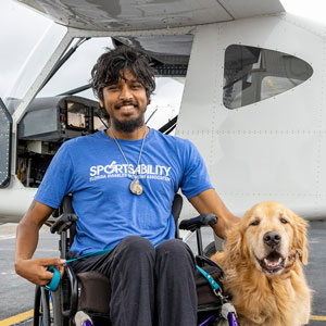 A man in a wheelchair, with a dog seated beside him, is pictured outside of an airplane.
