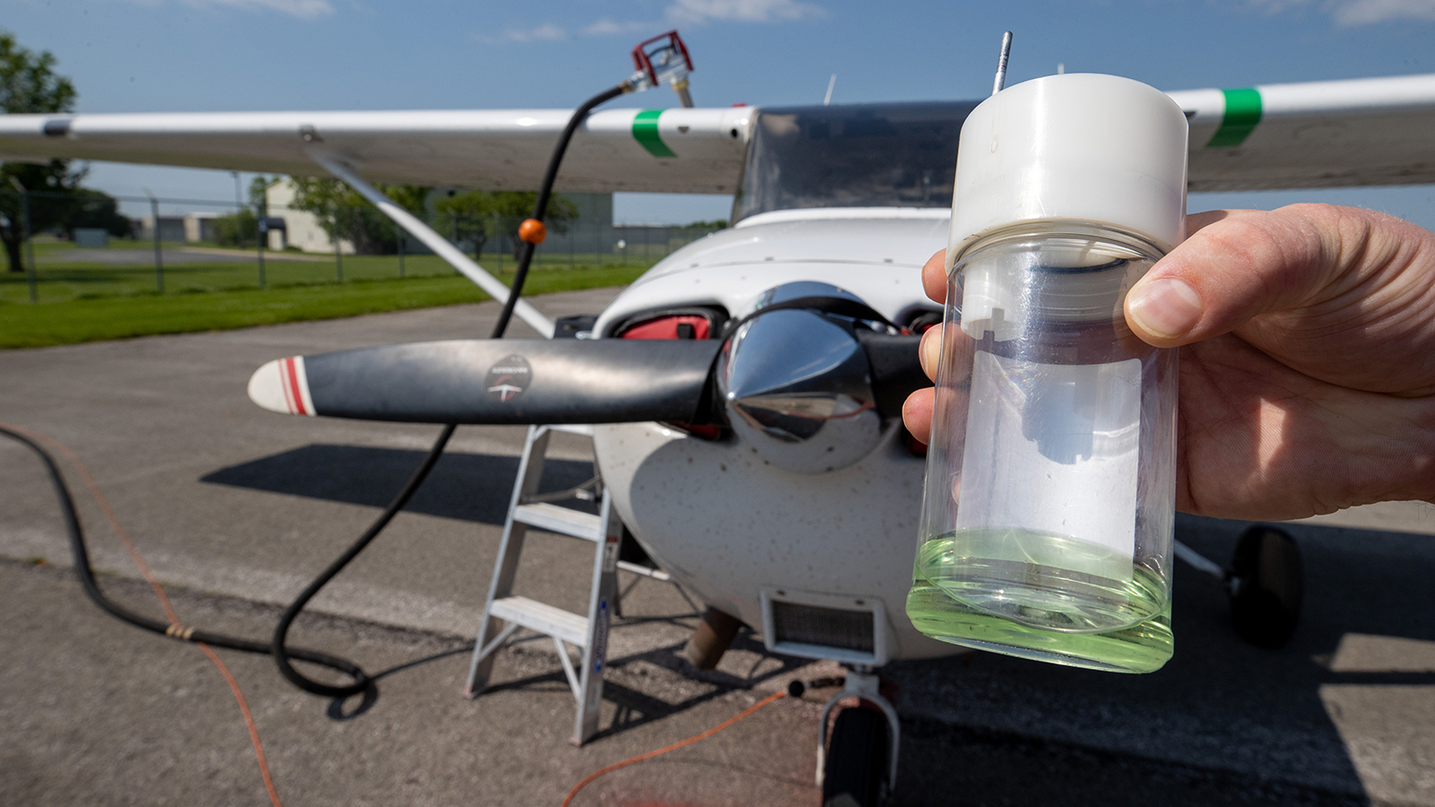 A container of fuel is being held and an airplane is visible in the background.