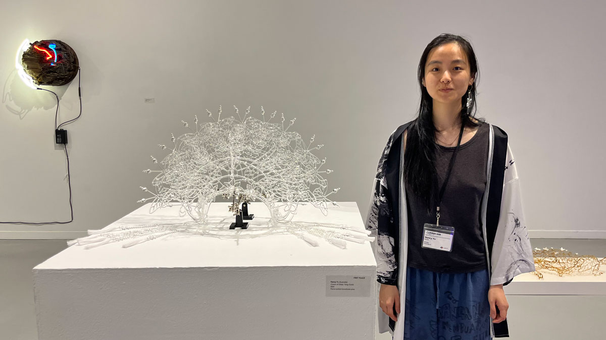 A woman stands next to a headdress made of glass.