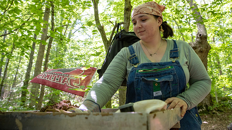A woman is screening dirt.