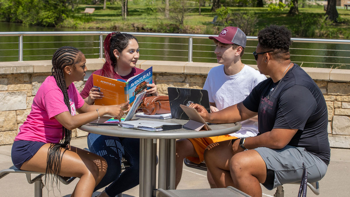Students sitting at an outdoors table collaborating on assignments