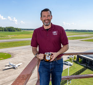 A man stands on a balcony overlooking a small airport.