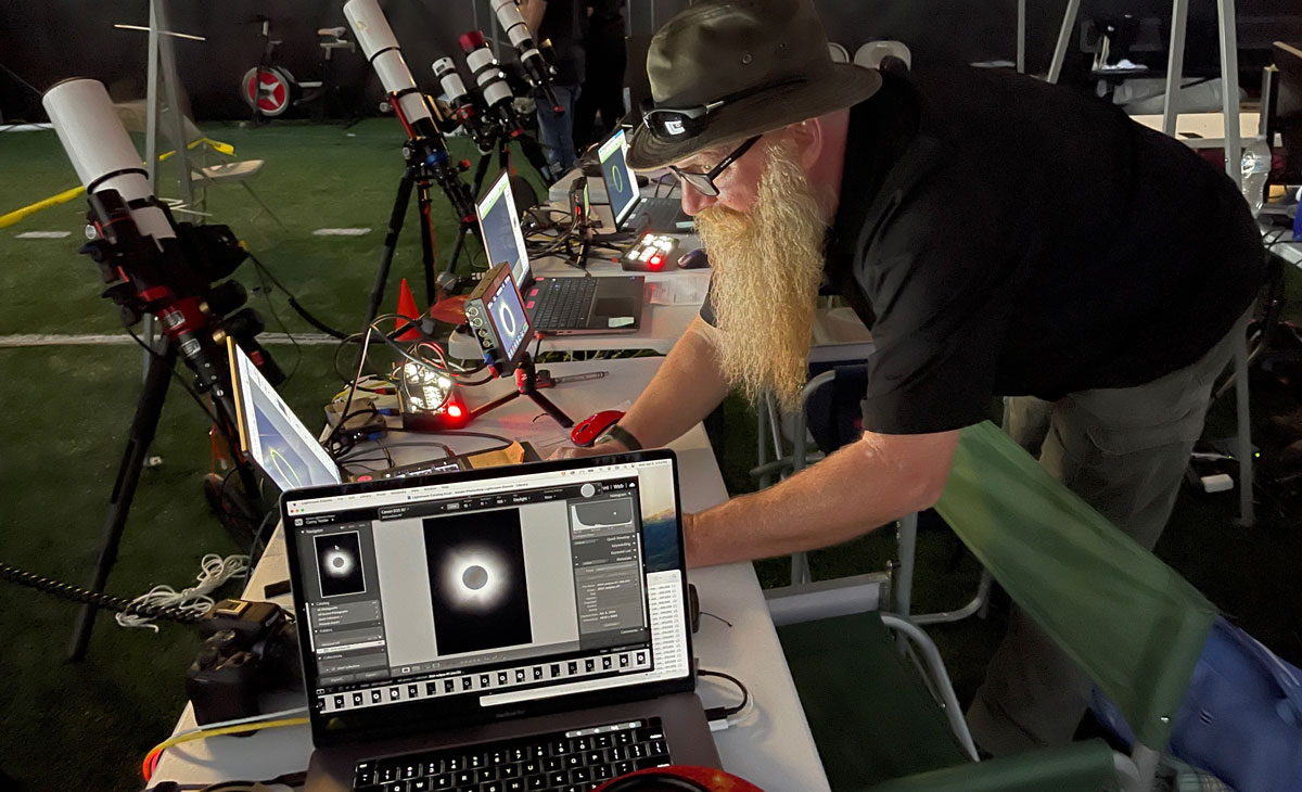 A man is looking at a computer during the eclipse. Telescopes are all around.
